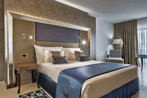 Hotelzimmer im AX The Palace mit einem großen Bett, Kissen, Tischlampe und Sessel.