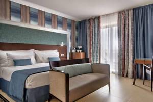 AX The Palace Hotel Zimmer mit Bett, Couch, Schreibtisch und Lampe