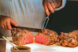 Koch im AX The Palace schneidet ein Steak mit einem Messer.