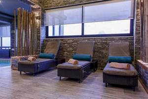 Spa-Lounge-Bereich im AX The Palace Hotel mit drei Liegen, die an einer Wand mit Steinmuster und Glasfenstern ausgerichtet sind.