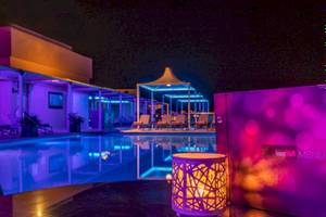 Nachtansicht des Swimmingpools des AX The Palace Hotels mit farbigen Lichtern und Loungestühlen.