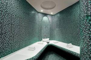Sauna im Sheraton Jumeirah Beach Resort mit grünen Mosaikwänden und weißen Liegeflächen.