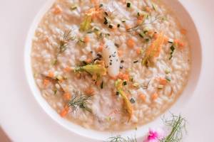 Eine Schüssel mit Risotto gefüllt mit Gemüse und Fisch, dekoriert mit Dill und Karotten.