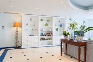 Empfangsbereich im Belvedere Luxury Suites mit weißen Regalen, Büchern, Vasen, einem Tisch und Pflanzen.