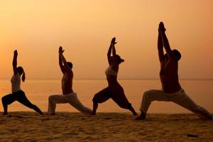 Vier Personen machen Yoga am Strand bei Sonnenuntergang.