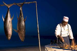 Koch am Grill mit frischen Thunfischen aufgehängt am Strand des Royal Zanzibar Beach Resort
