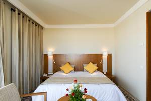 Schlafzimmer im Vincci Helios Beach Hotel mit zwei gelben Kissen und Blumen auf dem Tisch.