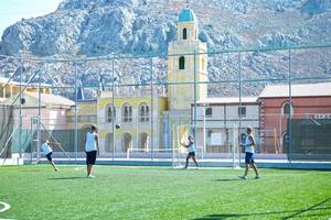 Fussballspieler spielen auf einem Fussballplatz im Freien vor einem historischen Gebäude.