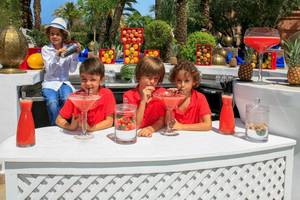 Kinder hinter einem Bartresen im Sofitel Marrakech Lounge & Spa mit selbstgemachten Getränken und Früchten im Hintergrund.