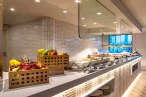 Frühstücksbuffet im Guayarmina Princess Hotel mit Obst, Tellern und Tischen.