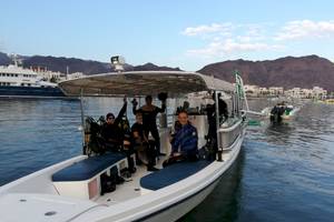 Taucher auf Boot vor Bergpanorama mit weiteren Booten im Hintergrund
