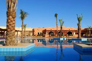 Außenpool des JAZ Neo Dar El Madina Hotels mit Palmen und orangefarbenem Gebäude.