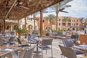 Restaurant-Terrasse im Jaz Neo Dar El Madina Hotel mit Tischen, Stühlen und Palmen im Hintergrund.