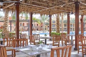 Außenbereich des Restaurants im JAZ Neo Dar El Madina Hotel mit runden Tischen und Stühlen unter einem Strohdach.