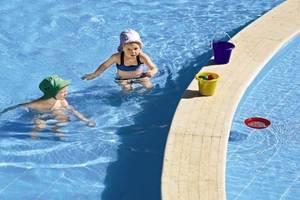 Zwei Kinder schwimmen im Pool des Jaz Dar El Madina Hotels, eines mit Hut und einer mit einem Eimer.