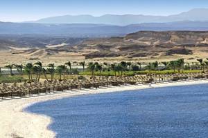 Luftaufnahme des Jaz Dar El Madina Hotels, Strand mit vielen Sonnenschirmen und Bergen im Hintergrund.