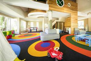 Das Kinderspielzimmer im Robinson Khao Lak Hotel mit bunten Teppichkreisen, Spielzeugautos und Spieltischen.