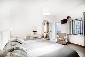 Hotelzimmer von Agali Houses mit weißem Bett, Stühlen, Tisch und Blick auf das Meer.