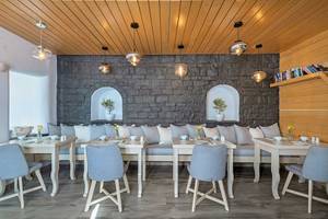 Innenansicht des Restaurants von Agali Houses mit steinerner Wand, Couch, Tischen und Stühlen.
