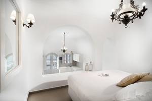 Schlafzimmer im Agali Houses mit weißen Wänden, einem großen Bett, einem Spiegel und Kronleuchtern.