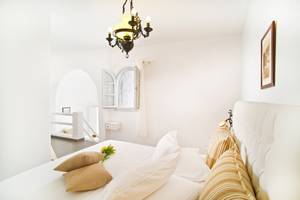Schlafzimmer im Agali Houses Hotel mit einem Bett, Kissen, Blumen und einem offenen Fenster.