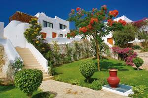 Außenbereich des Sharm Club Beach Resorts mit weißem Gebäude, Treppen und bunten Blumen.