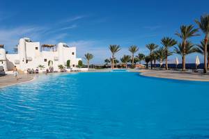 Ein großer Swimmingpool im Sharm Club Beach Resort mit weißen Gebäuden und Palmen im Hintergrund.