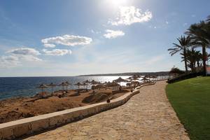 Strandweg des Sharm Club Beach Resort mit Sonnenschirmen und Blick auf das Meer.