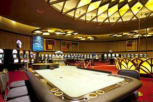 Ein Casino mit einem leeren Spieltisch und Spielautomaten im Hintergrund.