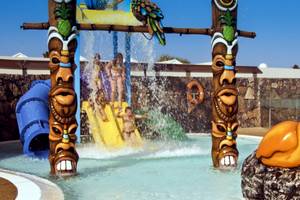 Kinder spielen auf dem Wasserspielplatz des HD Beach Resorts mit bunten Wasserrutschen und Tiki-Figuren.