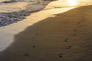 Strand des HD Beach Resorts bei Sonnenuntergang mit sichtbaren Fußabdrücken im Sand.