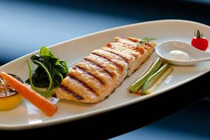 Gegrillter Lachs auf einem weißen Teller mit Spinat, Karotten, Zucchini, Zitrone und Tomatensauce.