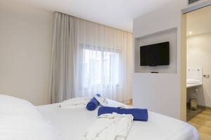 Ein modernes Zimmer im Occidental Playa de Palma mit einem Fernseher an der Wand und einem Bett mit weißen Laken.