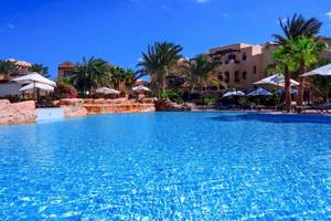 Pool im Steigenberger Coraya Beach Hotel mit Palmen und Gebäuden im Hintergrund.