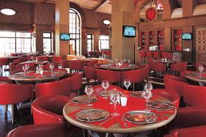 Restaurant im Cornelia Diamond Golf Resort & Spa mit roten Stühlen und Tischen, Fernsehgeräten und Weinflaschen.
