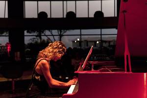 Eine Musikerin spielt ein rotes Klavier im Cornelia Diamond Golf Resort & Spa.
