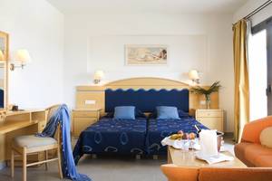Doppelzimmer im Atlantica Mikri Poli Rhodes Hotel mit zwei Betten, Schreibtisch und Obstkorb auf dem Tisch.