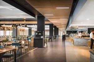 Innenansicht des Restaurants im Remisens Hotel Epidaurus mit Tischen, Stühlen und Angestellten, die Speisen zubereiten.