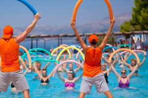 Schwimmkurs im Pool im Remisens Hotel Epidaurus mit Teilnehmern und Trainern, die Schwimmreifen halten.
