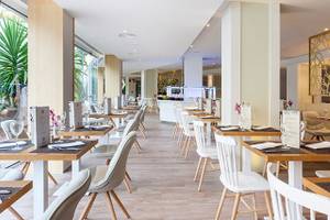 Innenansicht eines Restaurants im Hotel Tigotan Lovers & Friends mit Holztischen und weißen Stühlen.