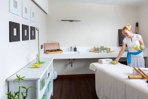 Eine Frau in einem weißen Kleid bereitet einen Massagetisch im Tigotan Lovers & Friends Hotel vor.