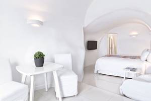 Weißes Schlafzimmer mit Bett, Tisch, Stühlen und Pflanzen im Katikies Chromata Santorini Hotel.