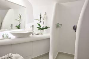 Badezimmer des Katikies Chromata Santorini Hotels mit weißem Waschbecken und Orchideen.