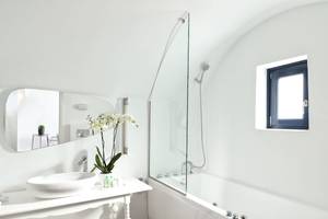 Ein Badezimmer im Katikies Chromata Santorini Hotel mit einer weißen Wanne, einem Waschbecken und einem Spiegel.