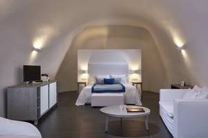 Ein modernes Schlafzimmer im Katikies Chromata Santorini Hotel mit weißem Bett, Nachttischen und einem Fernseher.