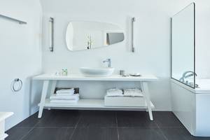Badezimmer im Katikies Chromata Santorini Hotel mit weißem Waschtisch und Dusche.