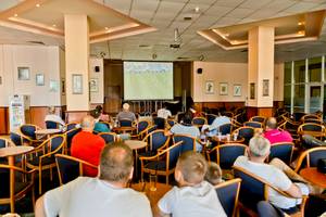 Gäste im DIT Evrika Beach Club Hotel sehen sich ein Fußballspiel auf einer Leinwand an.