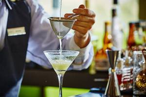 Ein Barkeeper bereitet einen Cocktail in einem Glas zu, indem er eine Flüssigkeit durch ein Sieb gießt.