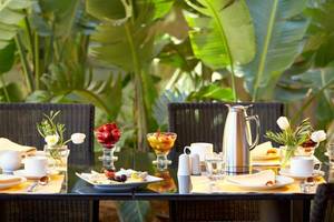 Frühstückstisch im Garten des Daios Cove Luxury Resort & Villas mit Früchten und Kaffeeservice.