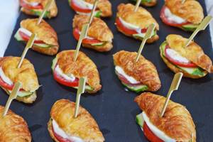 Eine Auswahl an Croissants mit Tomaten, Gurken und Mozzarella auf einem schwarzen Tablett.